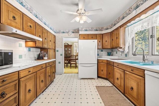 kitchen with white appliances, light floors, a sink, under cabinet range hood, and brown cabinets