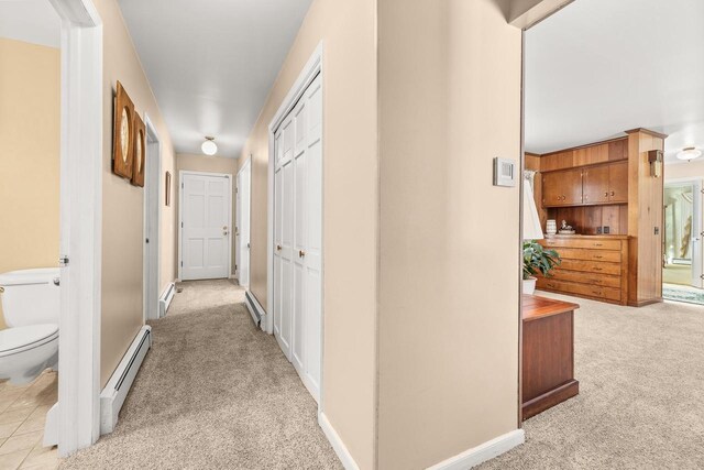 hallway with light carpet, a baseboard heating unit, and baseboards