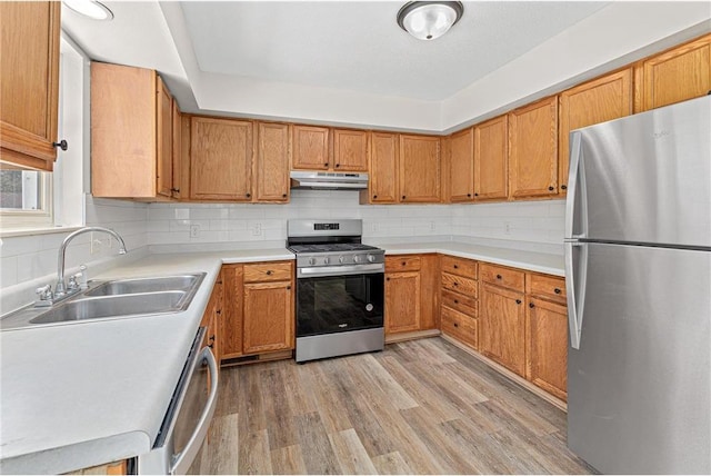 kitchen featuring light wood-style flooring, under cabinet range hood, a sink, stainless steel appliances, and decorative backsplash