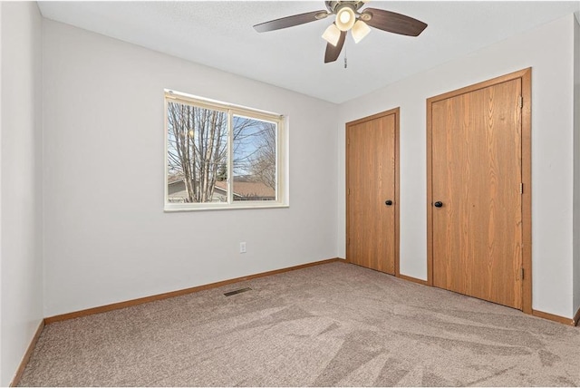 unfurnished bedroom with baseboards, visible vents, carpet floors, ceiling fan, and multiple closets