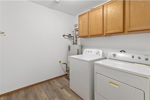 clothes washing area featuring baseboards, gas water heater, light wood-style floors, cabinet space, and independent washer and dryer