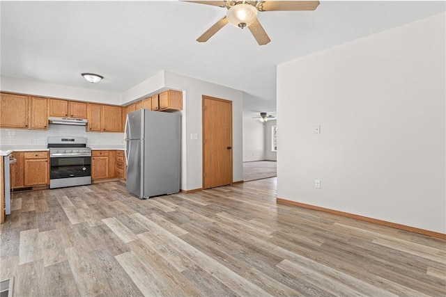 kitchen featuring under cabinet range hood, light countertops, light wood-type flooring, decorative backsplash, and appliances with stainless steel finishes