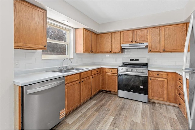 kitchen with backsplash, under cabinet range hood, light wood-type flooring, appliances with stainless steel finishes, and a sink