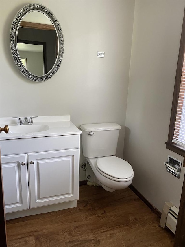 half bathroom with vanity, wood finished floors, baseboards, toilet, and baseboard heating