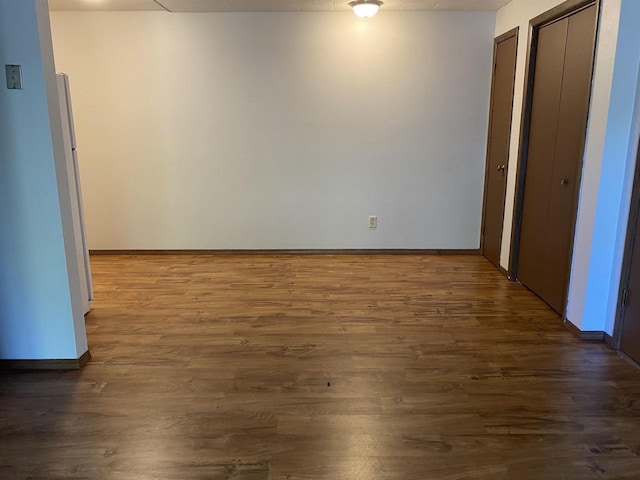 unfurnished bedroom with dark wood-type flooring, baseboards, and multiple closets