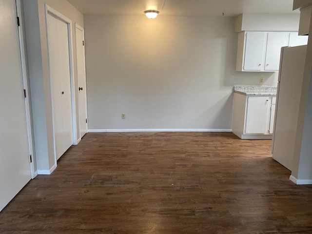 unfurnished dining area featuring baseboards and dark wood-style flooring