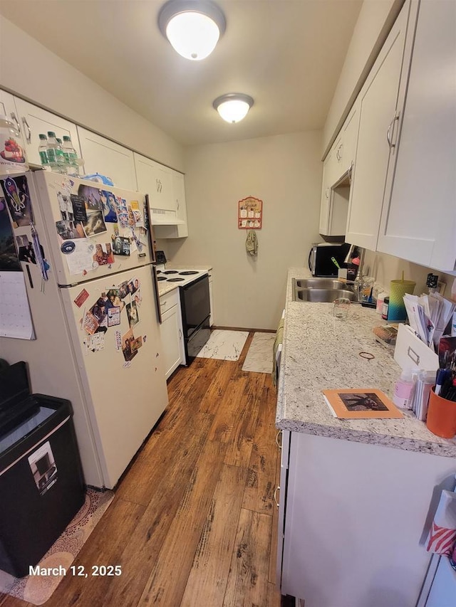 kitchen with light countertops, electric range oven, freestanding refrigerator, wood finished floors, and a sink