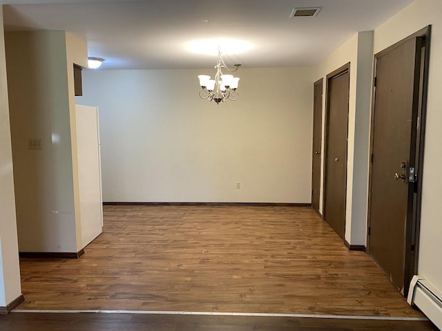 unfurnished dining area with visible vents, baseboards, wood finished floors, a notable chandelier, and a baseboard radiator