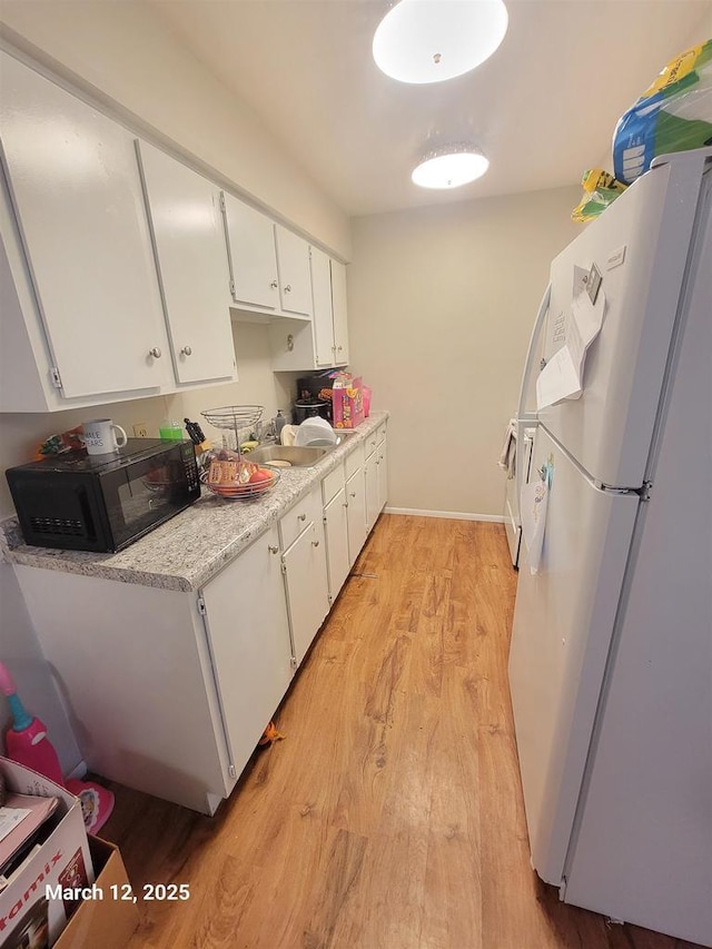 kitchen with light wood-style flooring, a sink, freestanding refrigerator, black microwave, and light countertops