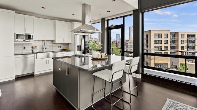 kitchen with a center island, decorative backsplash, appliances with stainless steel finishes, island range hood, and a sink