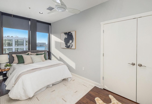 bedroom with visible vents, a ceiling fan, wood finished floors, a wall of windows, and baseboards