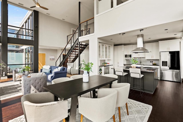 dining area with a ceiling fan, expansive windows, stairs, a high ceiling, and dark wood-style flooring