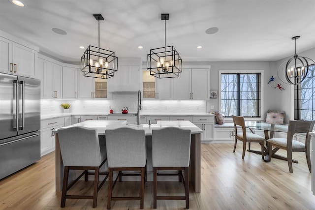 kitchen featuring light wood-type flooring, light countertops, built in fridge, an inviting chandelier, and a sink