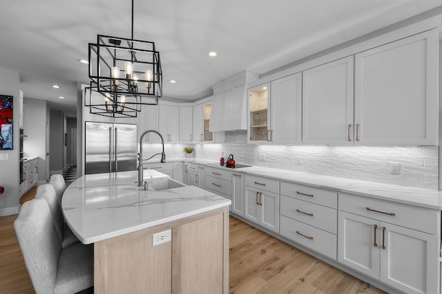 kitchen featuring light stone countertops, a sink, stainless steel built in fridge, backsplash, and a chandelier