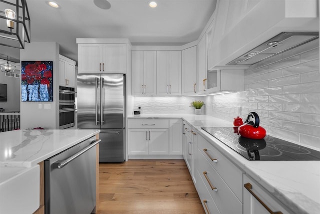 kitchen featuring light stone countertops, stainless steel appliances, light wood-style floors, exhaust hood, and white cabinetry