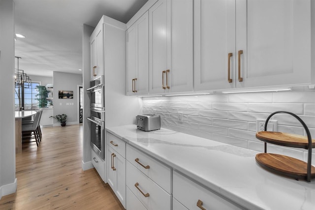 kitchen with light stone countertops, light wood finished floors, decorative backsplash, white cabinets, and double oven