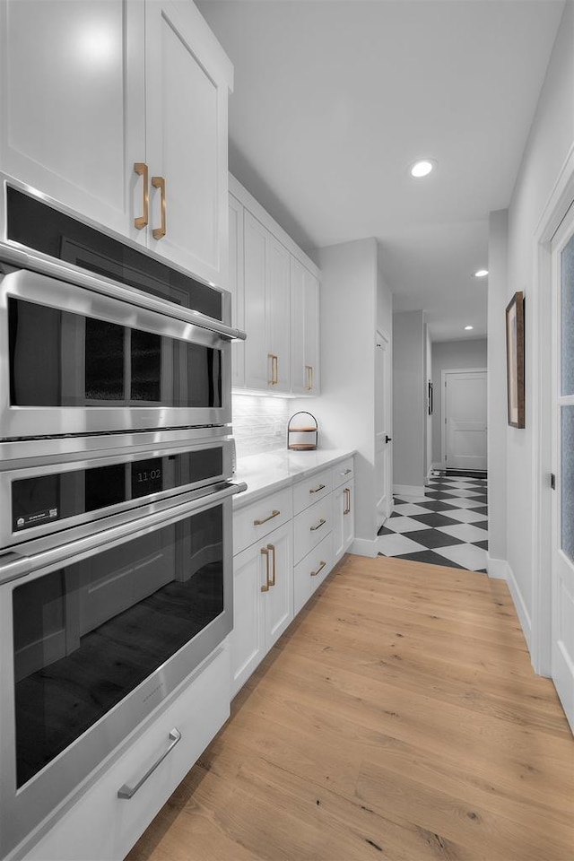 kitchen featuring double oven, light countertops, decorative backsplash, recessed lighting, and white cabinetry