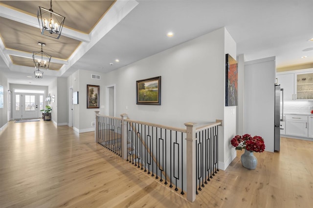 corridor with an upstairs landing, visible vents, light wood-style floors, and an inviting chandelier