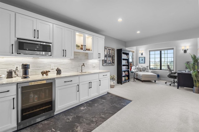 kitchen with a sink, stainless steel microwave, beverage cooler, and white cabinetry