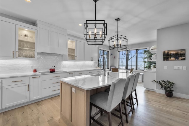 kitchen with an island with sink, light wood-style floors, black electric stovetop, backsplash, and a chandelier