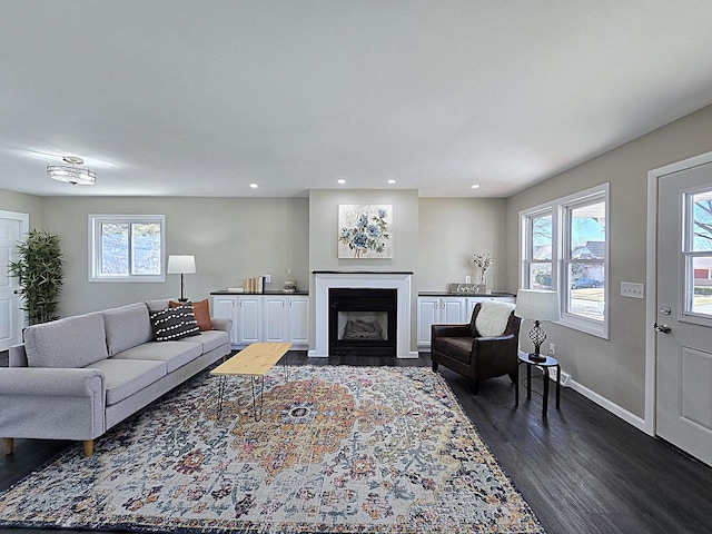 living room with a wealth of natural light, baseboards, a fireplace with flush hearth, and dark wood-style floors