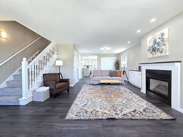 living area featuring stairway, dark wood-style floors, baseboards, a fireplace with flush hearth, and recessed lighting