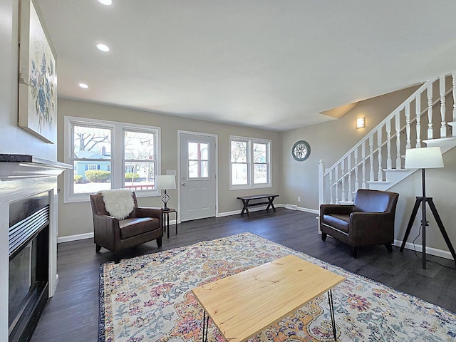 living room featuring stairway, dark wood-style floors, baseboards, recessed lighting, and a glass covered fireplace