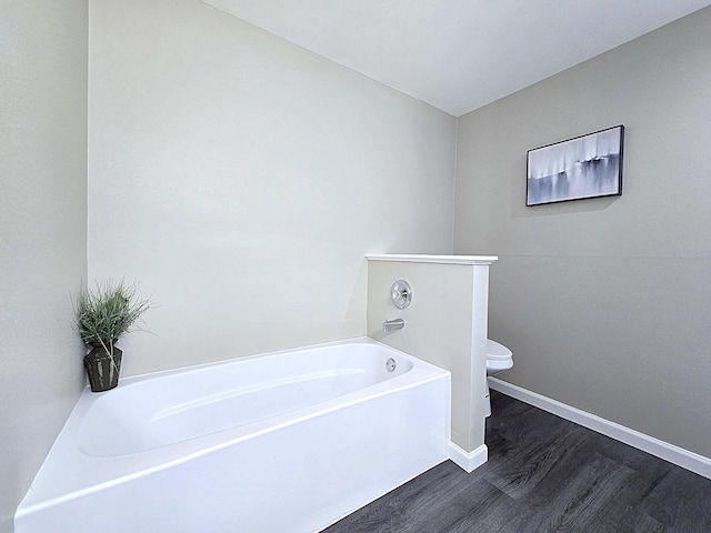 bathroom with baseboards, wood finished floors, toilet, and a bath