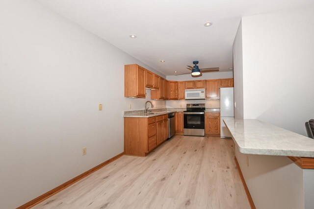 kitchen featuring baseboards, a peninsula, light wood-style flooring, a sink, and appliances with stainless steel finishes