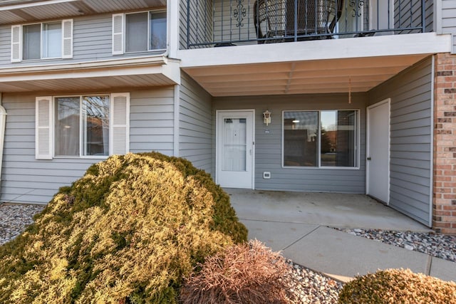 view of exterior entry with a patio, a balcony, and brick siding