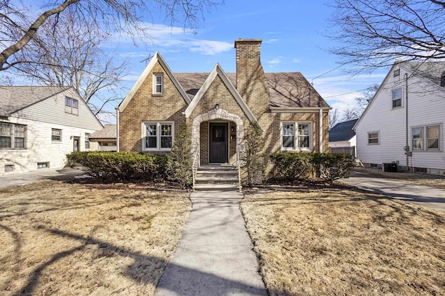 tudor home with central air condition unit, brick siding, and a chimney