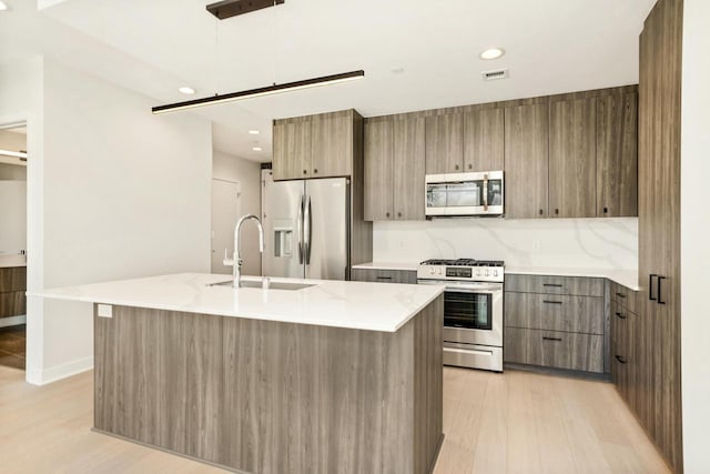 kitchen with light wood finished floors, a kitchen island with sink, a sink, stainless steel appliances, and modern cabinets