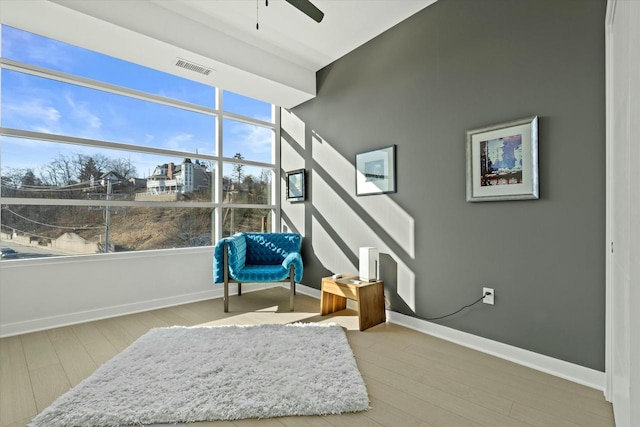 living area featuring visible vents, baseboards, ceiling fan, and wood finished floors