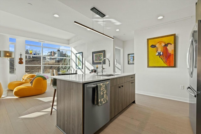 kitchen featuring a sink, light countertops, light wood-style flooring, appliances with stainless steel finishes, and a kitchen island with sink