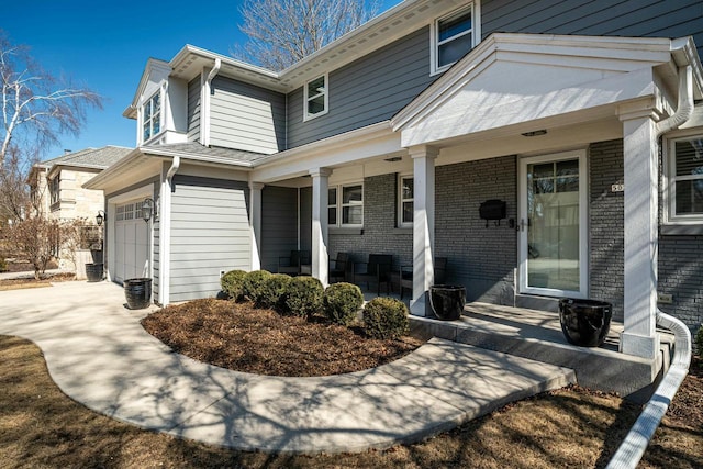 view of side of home with a porch, a garage, brick siding, and driveway