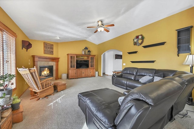 living area with arched walkways, ceiling fan, vaulted ceiling, a tiled fireplace, and carpet flooring