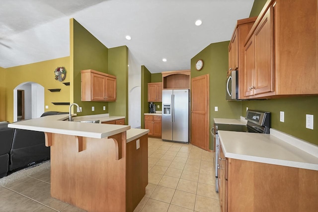 kitchen featuring light tile patterned floors, a peninsula, a sink, stainless steel appliances, and a kitchen bar