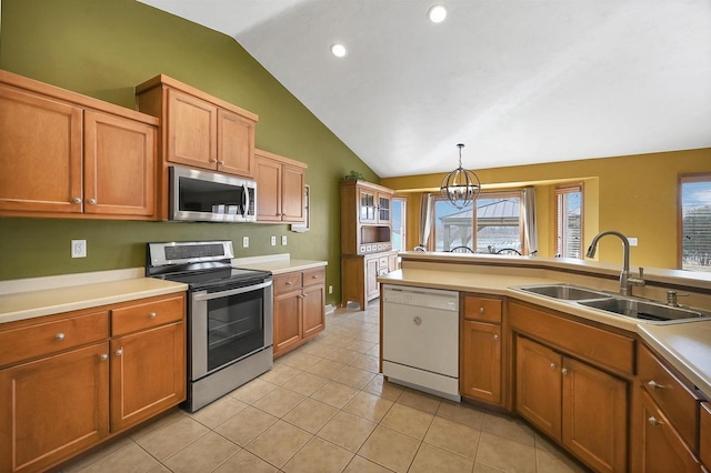 kitchen featuring brown cabinets, a sink, decorative light fixtures, appliances with stainless steel finishes, and vaulted ceiling