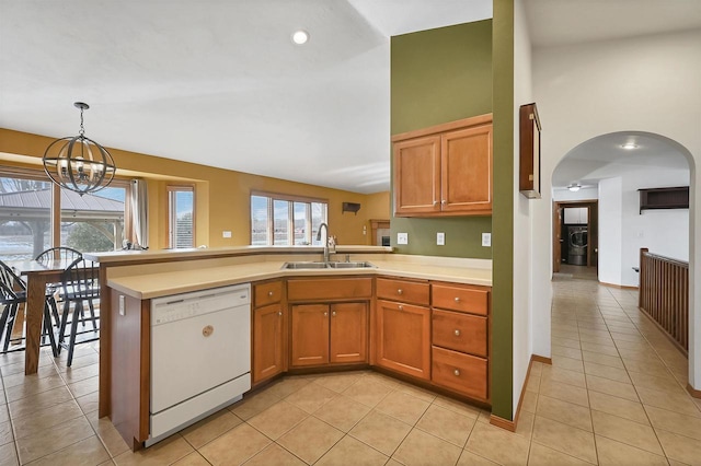 kitchen with light countertops, a peninsula, white dishwasher, arched walkways, and a sink