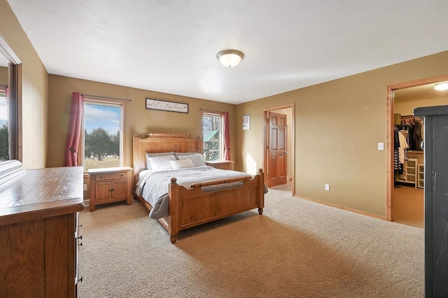 bedroom featuring baseboards, multiple windows, light colored carpet, and a spacious closet