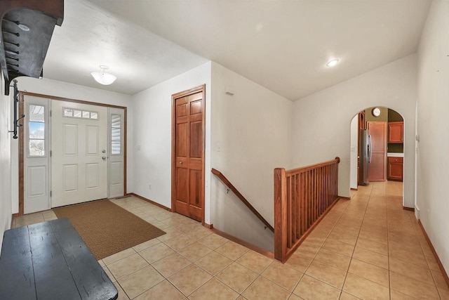 foyer entrance featuring lofted ceiling, light tile patterned floors, baseboards, and arched walkways