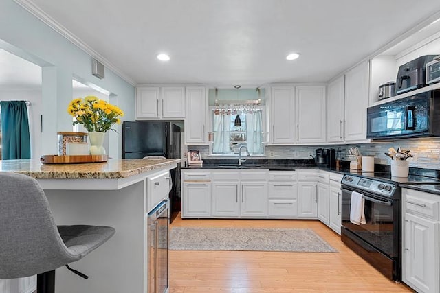 kitchen featuring white cabinetry, black appliances, decorative backsplash, and a sink