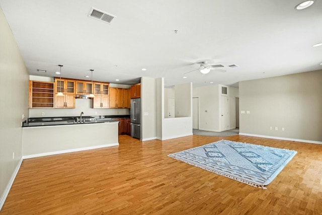 unfurnished living room with visible vents, light wood-style flooring, ceiling fan, and a sink