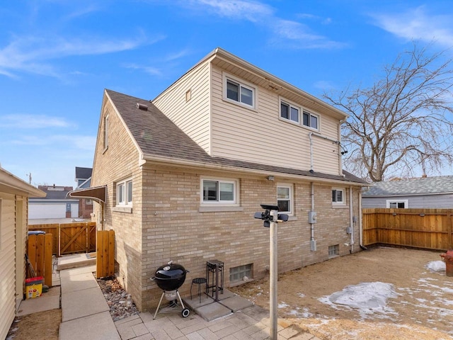 back of property with a patio, a fenced backyard, brick siding, and roof with shingles