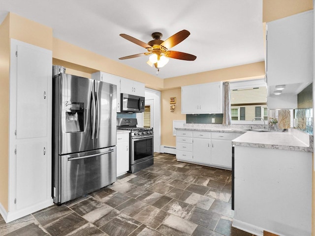 kitchen featuring stone finish flooring, a baseboard heating unit, white cabinetry, appliances with stainless steel finishes, and light countertops