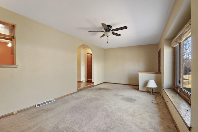 carpeted spare room with arched walkways, visible vents, baseboards, and a ceiling fan