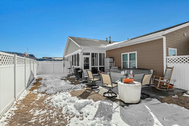 snow covered rear of property featuring a patio area, a fenced backyard, and a sunroom