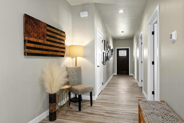 hallway with a textured ceiling, light wood-type flooring, and baseboards