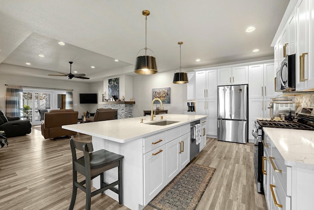 kitchen with open floor plan, light wood-type flooring, appliances with stainless steel finishes, white cabinetry, and a sink