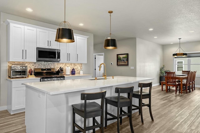 kitchen featuring a center island with sink, decorative backsplash, light wood-style flooring, stainless steel appliances, and a sink